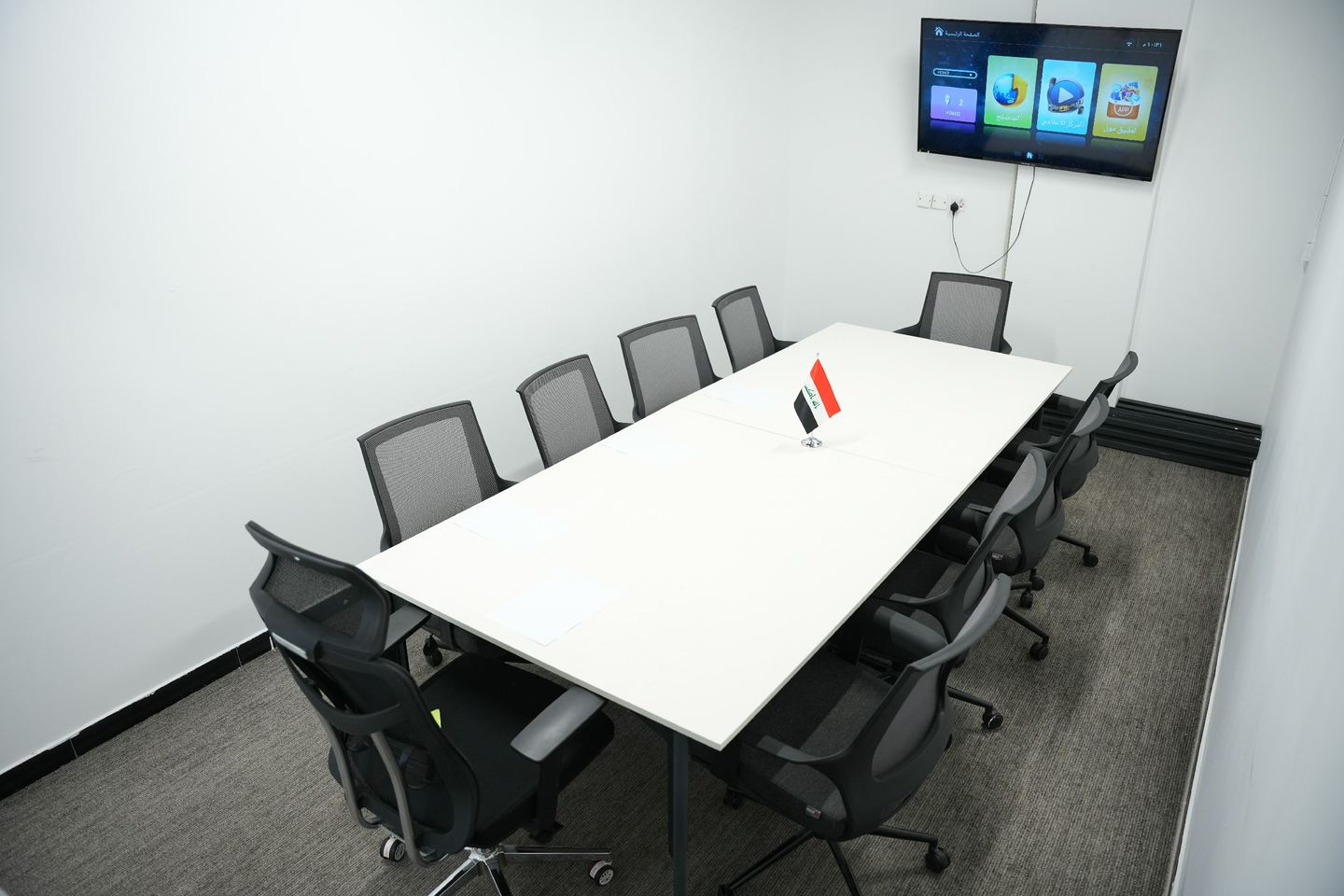 Boardroom with a long white table, eight chairs and a wall-mounted display